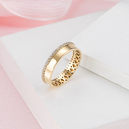 A gold ring with a diamond-encrusted band is displayed on a white surface against a pink background.