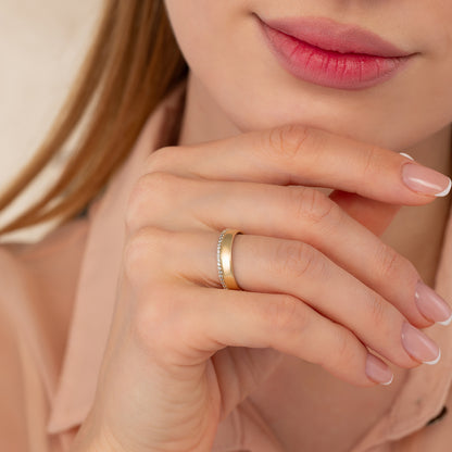 A close-up of a person's hand wearing a gold ring, with their chin resting on their hand.