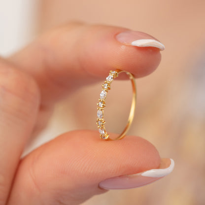 A close-up image of a person's hand holding a delicate gold ring with a row of small diamonds.