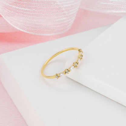 A gold ring with a decorative band of small diamonds is displayed on a white surface against a pink background.