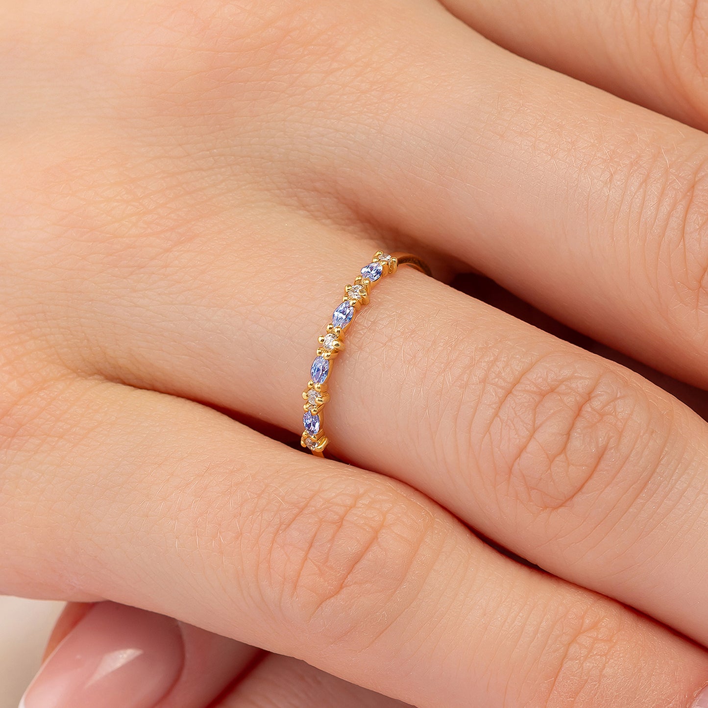 A close-up image of a person's hand wearing a gold ring with blue stones.