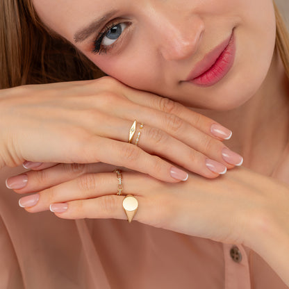 A close-up of a woman's face, with her hands resting on her face and wearing multiple rings on her fingers.