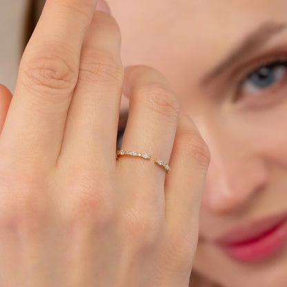 A close-up of a person's hand wearing a gold ring with small diamonds, with a blurred background of a person's face.