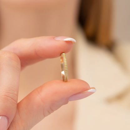 A person's hand holding a small gold ring with a thin band.