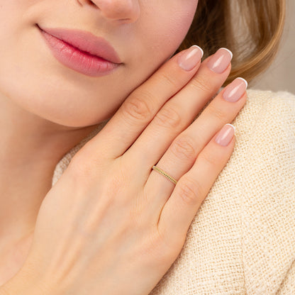 A close-up of a person's hand wearing a gold ring, with their fingers gently curled around their body.