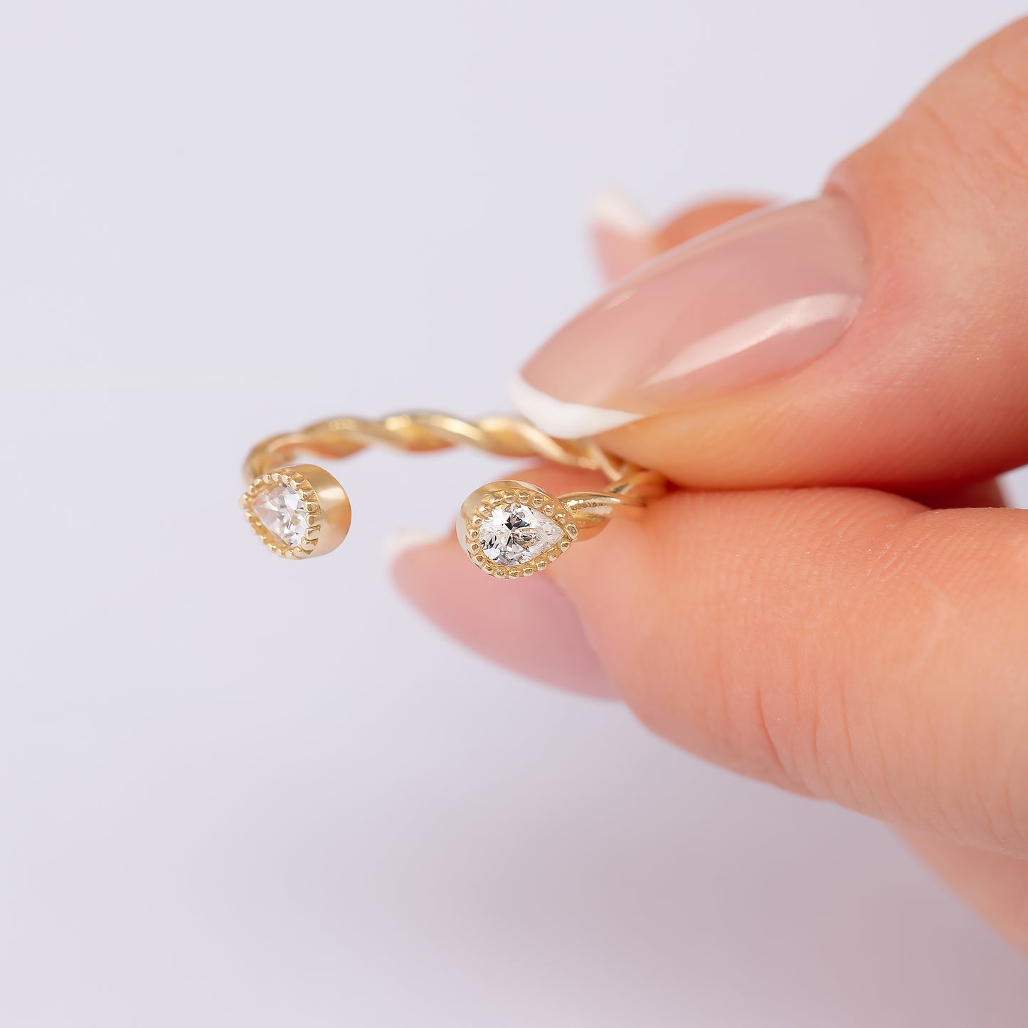 A close-up image of a person's hand holding a gold ring with two diamond-encrusted stones.