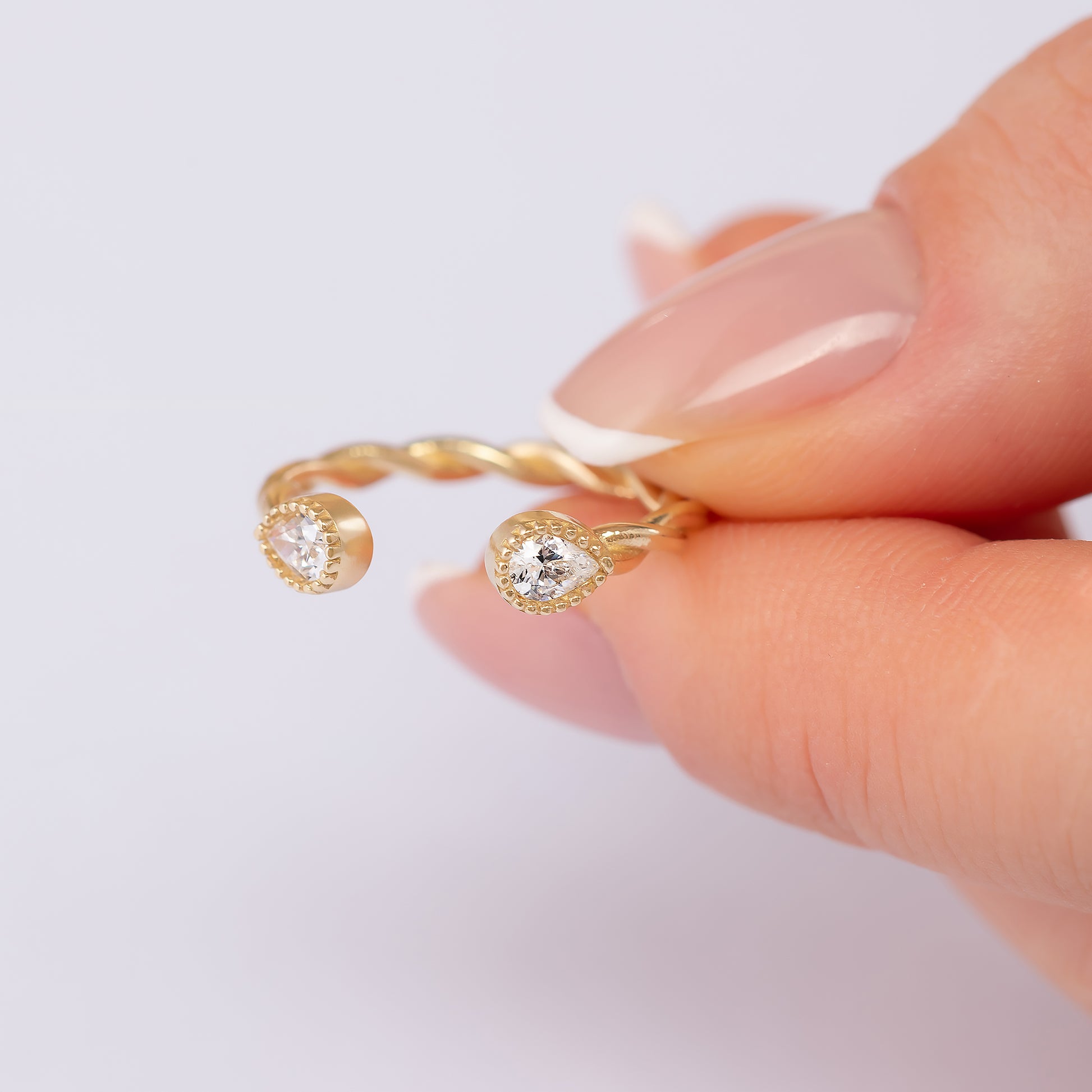 A close-up image of a person's hand holding a gold ring with two diamond-encrusted stones.