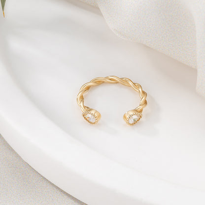 A gold ring with a twisted design and two small diamonds on either side rests on a white surface.