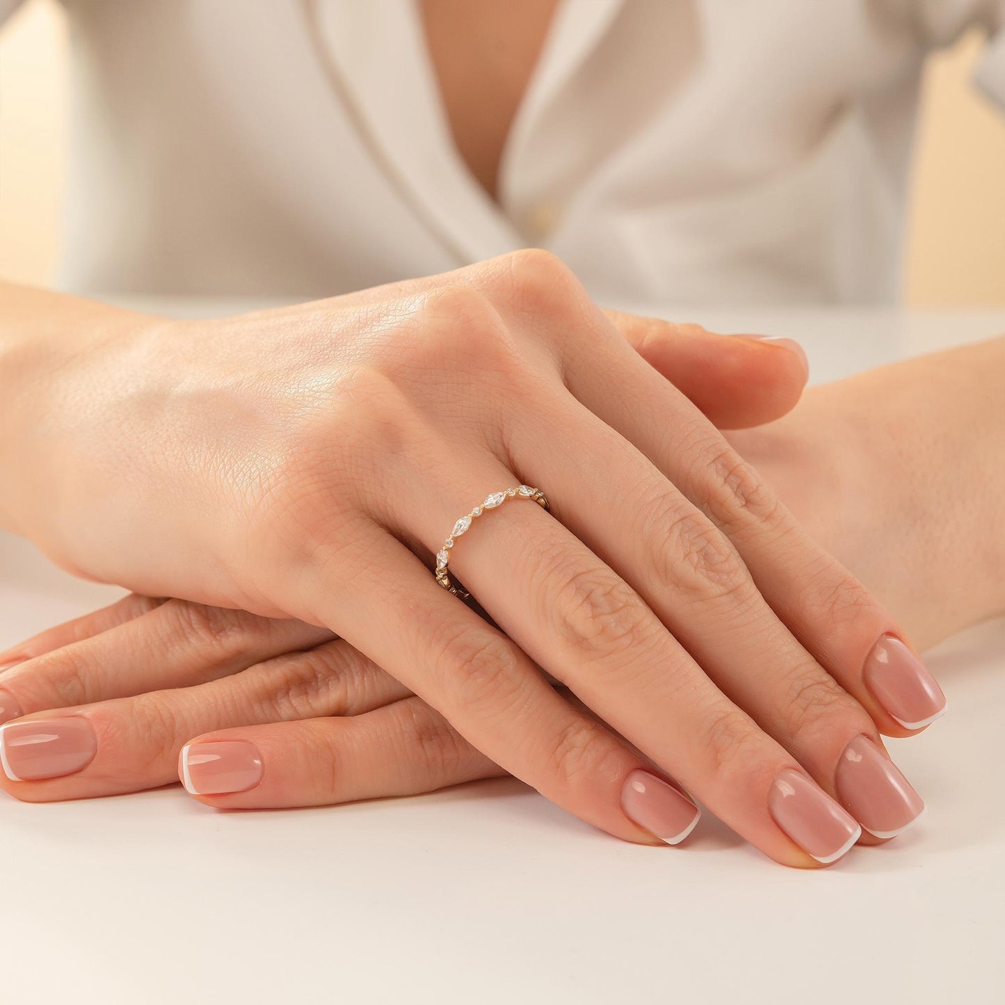 A close-up image of a person's hands with a ring on the finger, resting on a white surface.