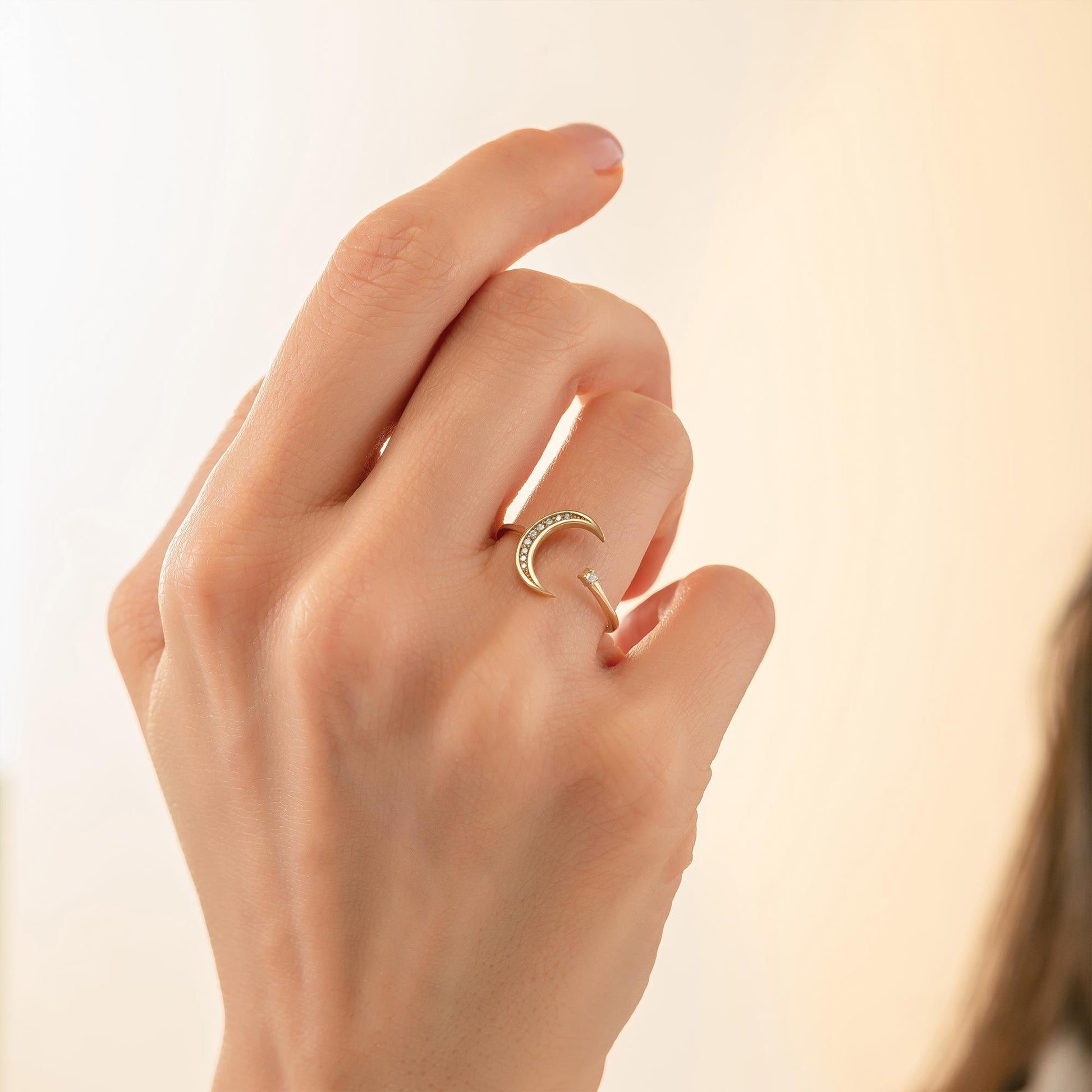 A close-up of a person's hand wearing a gold ring with a crescent moon design.