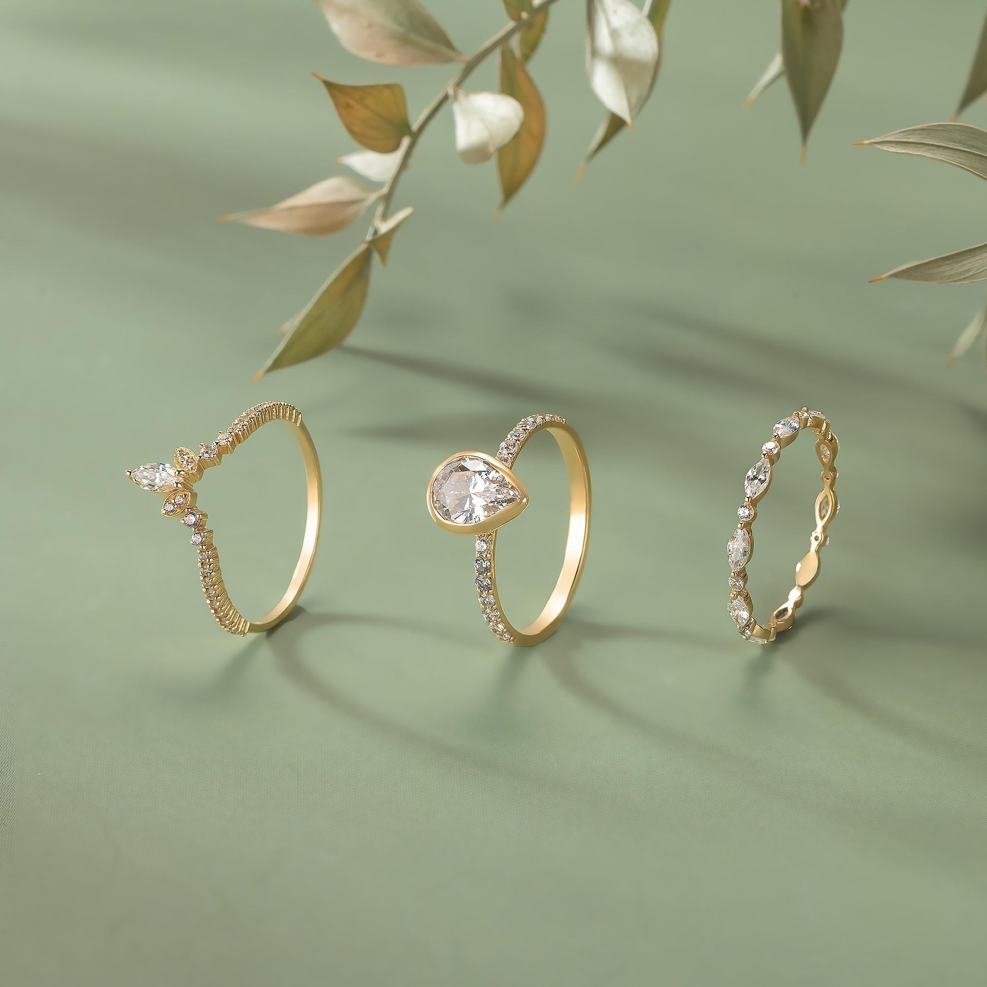 Three gold rings with diamonds are displayed on a green background, with a branch of leaves in the background.