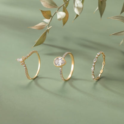 Three gold rings with diamonds are displayed on a green background, with a branch of leaves in the background.