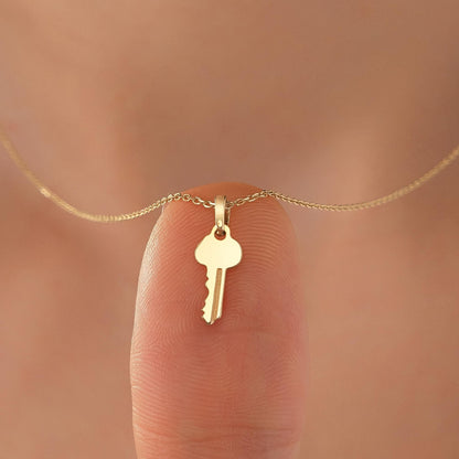 A small gold-colored key charm is attached to a delicate chain necklace.