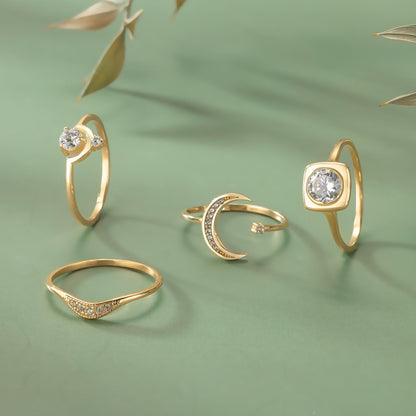 a collection of four gold rings with various designs, including a crescent moon and a square cut gemstone.