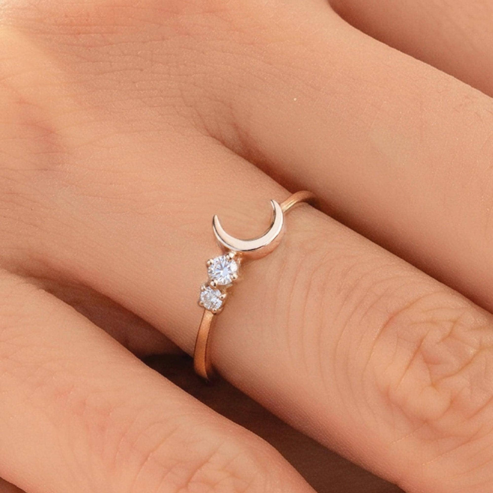 A close-up of a person's hand wearing a gold ring with a crescent moon and two small diamonds.