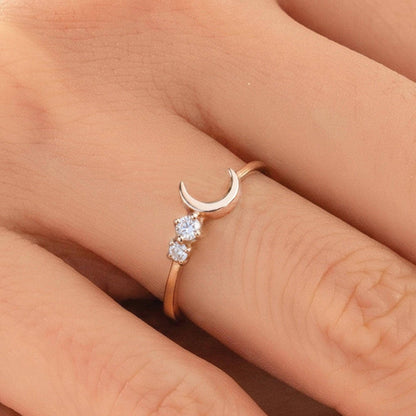 A close-up of a person's hand wearing a gold ring with a crescent moon and two small diamonds.