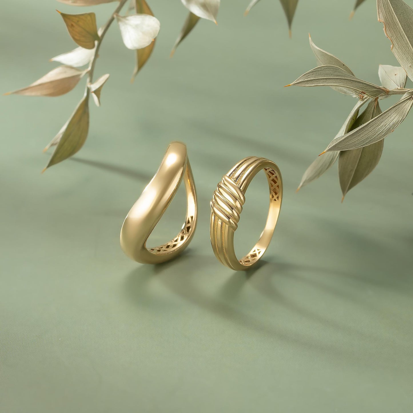 Two gold rings are displayed on a green background, with a branch of leaves in the background.