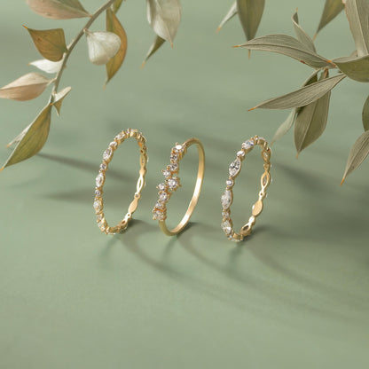 Three gold rings with intricate designs and sparkling gemstones are displayed against a green background, with some leaves visible in the background.