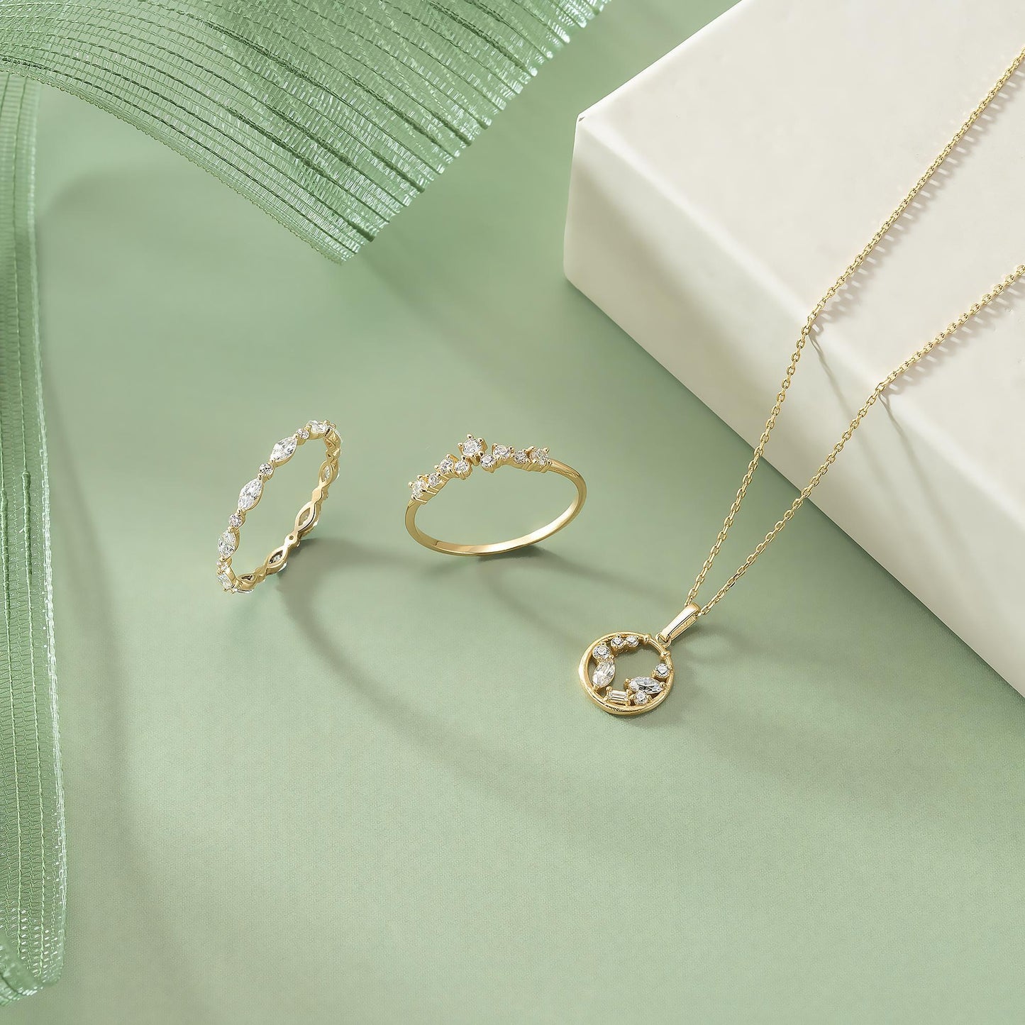 a collection of three pieces of jewelry, including rings and a necklace, arranged on a green background.