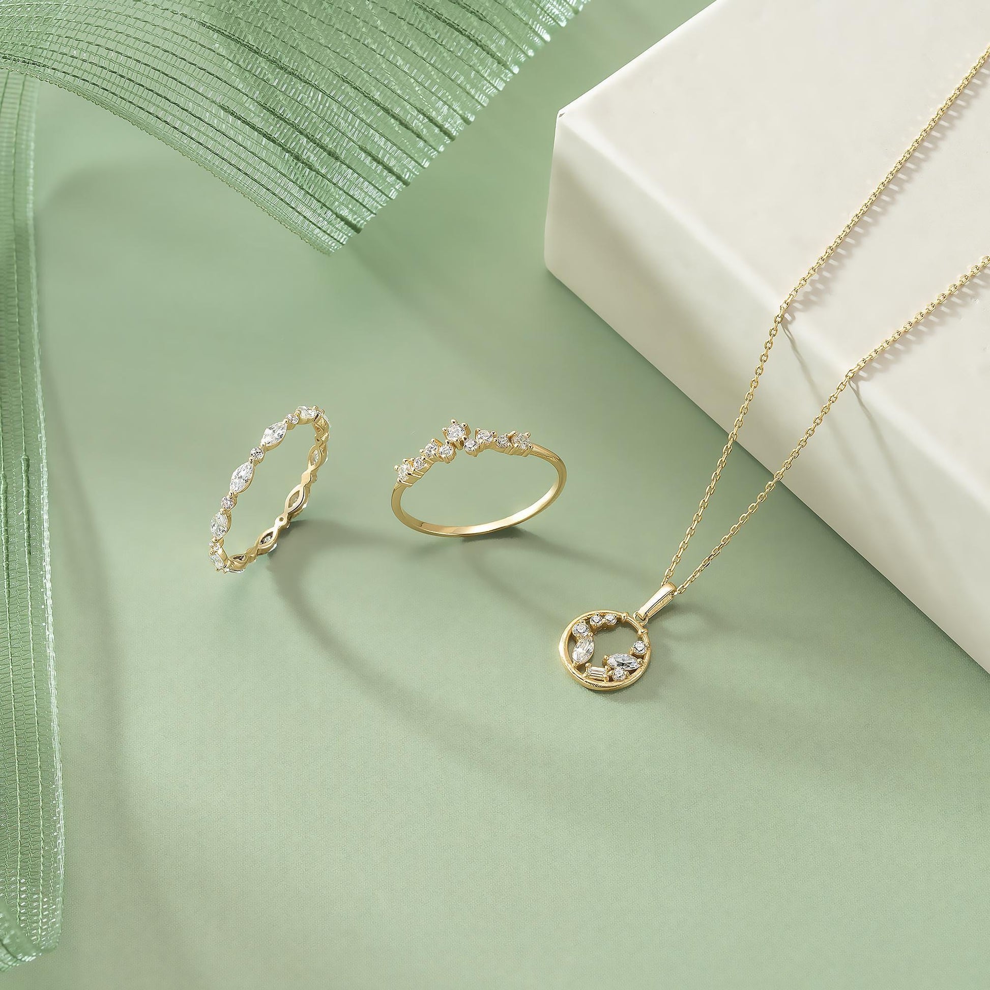 a collection of three pieces of jewelry, including rings and a necklace, arranged on a green background.
