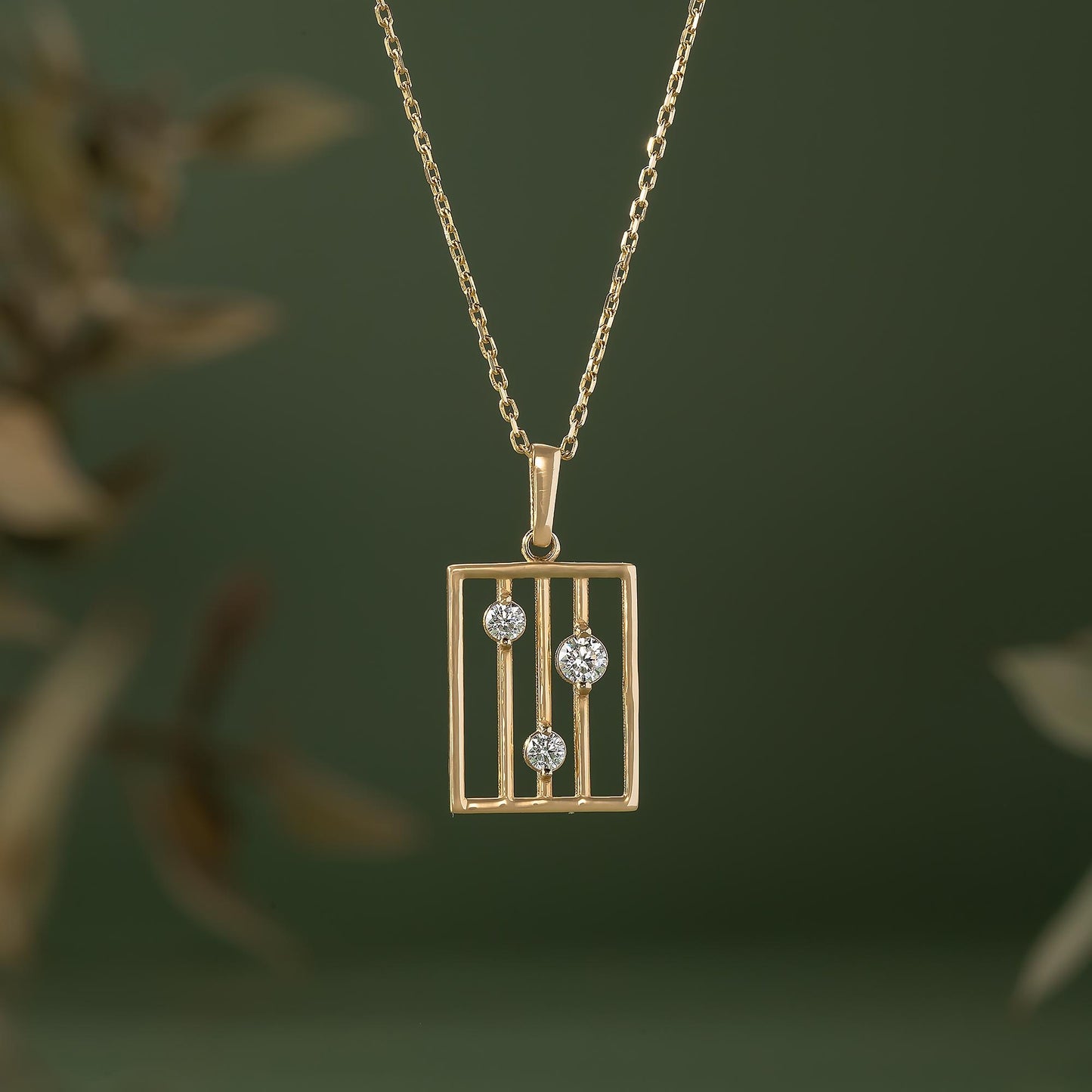 A gold-colored necklace with a rectangular pendant featuring three diamonds set within a gold-colored metal frame.