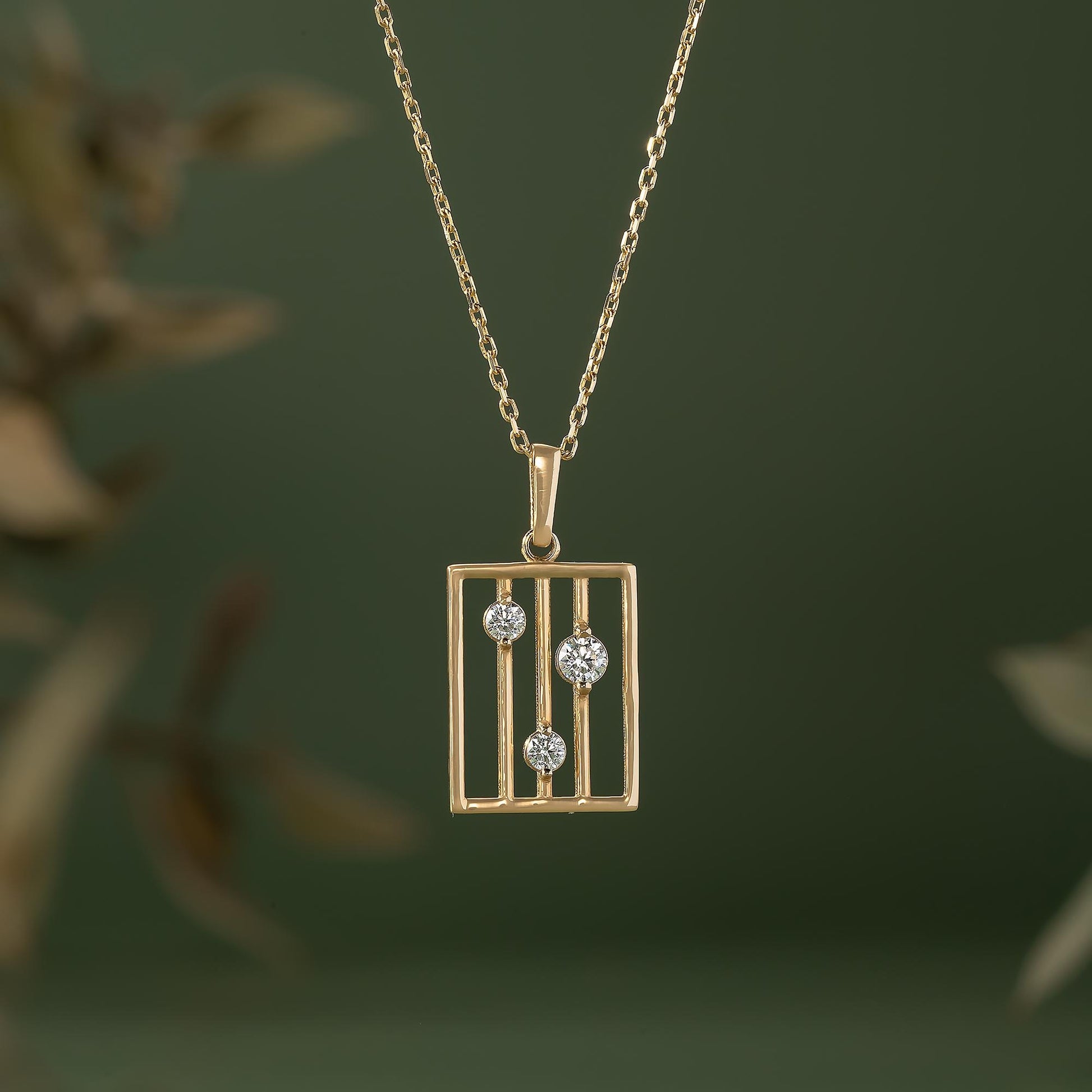 A gold-colored necklace with a rectangular pendant featuring three diamonds set within a gold-colored metal frame.