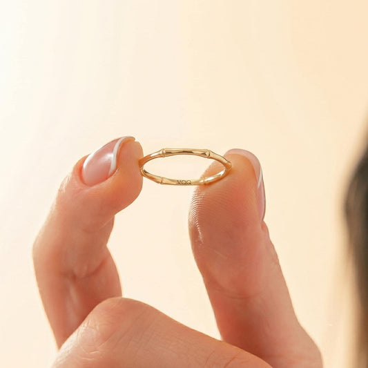 A person's hand holding a small gold ring with a unique design.