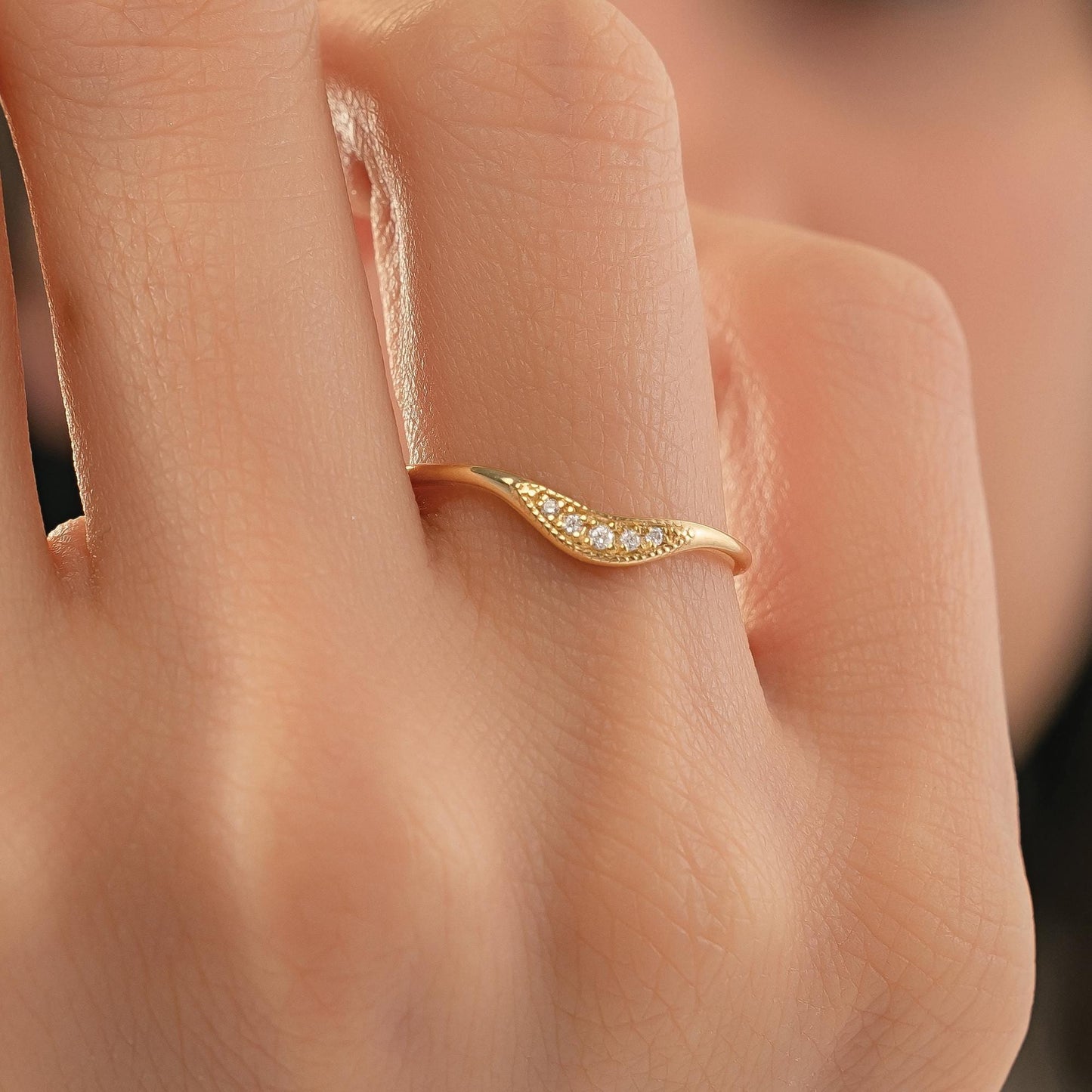 A close-up of a person's hand wearing a gold ring with a small diamond accent.