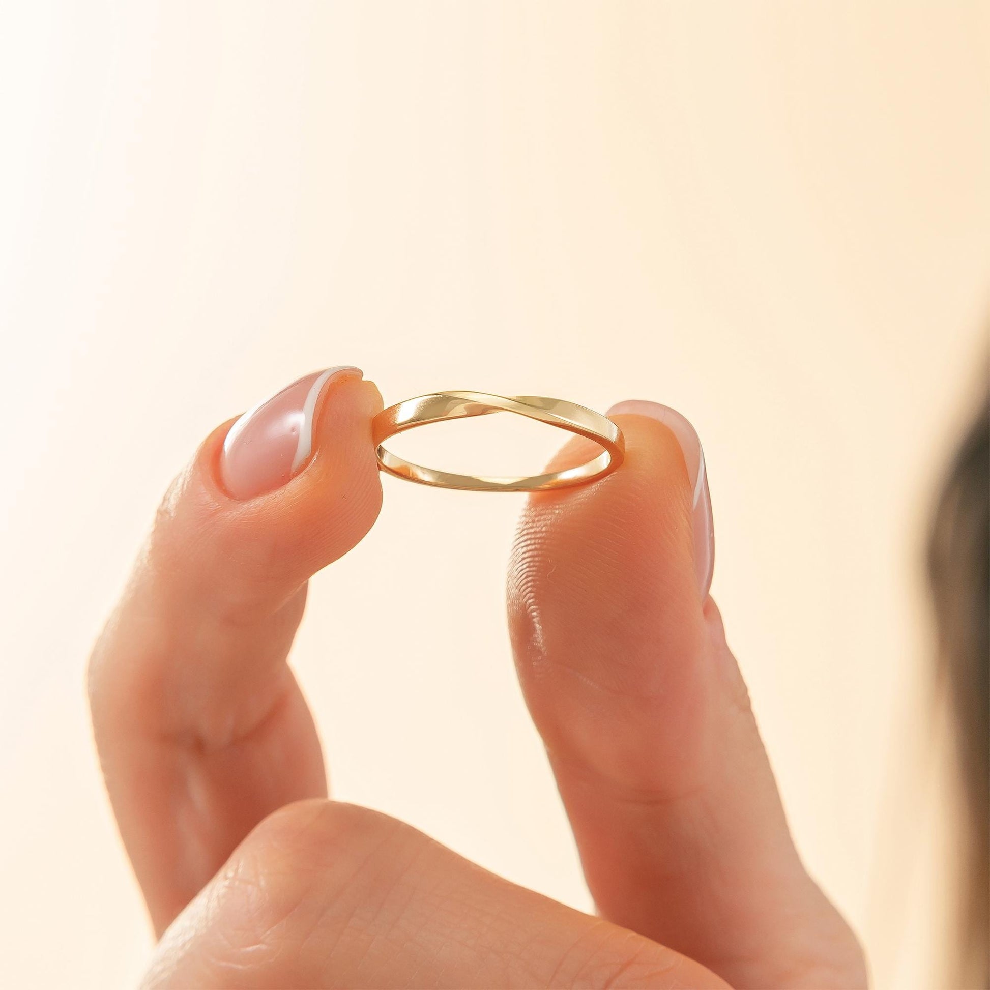 A person's hand holding a gold ring with a twisted design.
