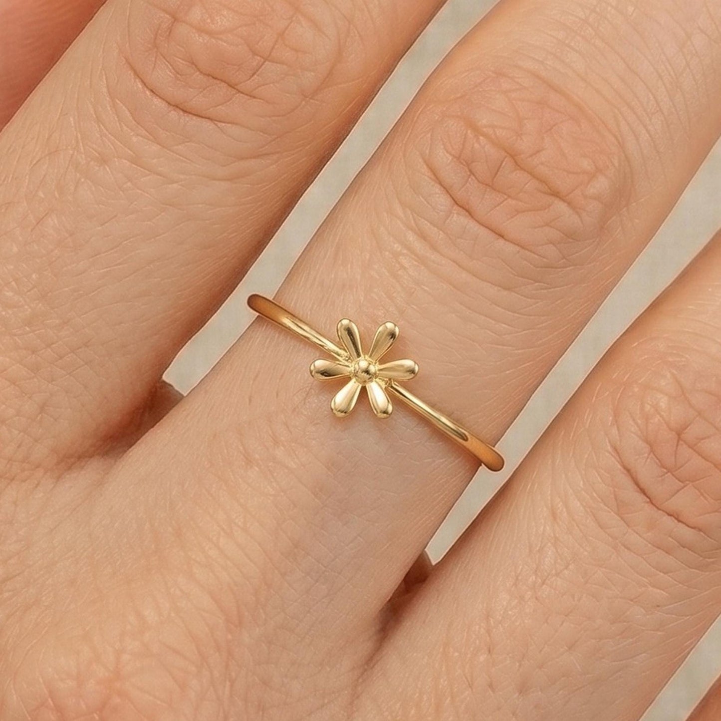 A gold ring with a small flower design on the band is shown on a person's hand.