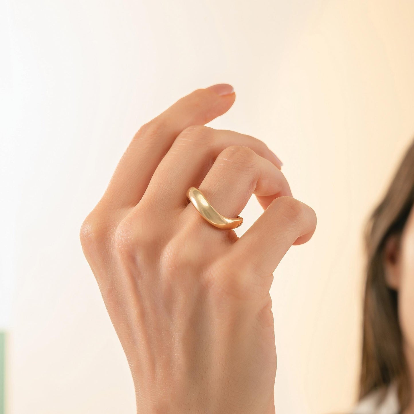 A close-up of a person's hand wearing a gold ring, with a blurred background.