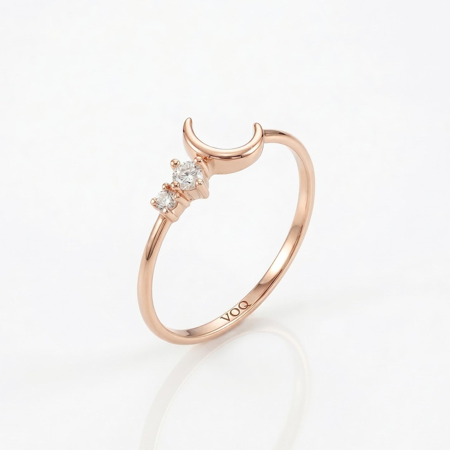 A rose gold ring with a crescent moon and three small diamonds set in the center.