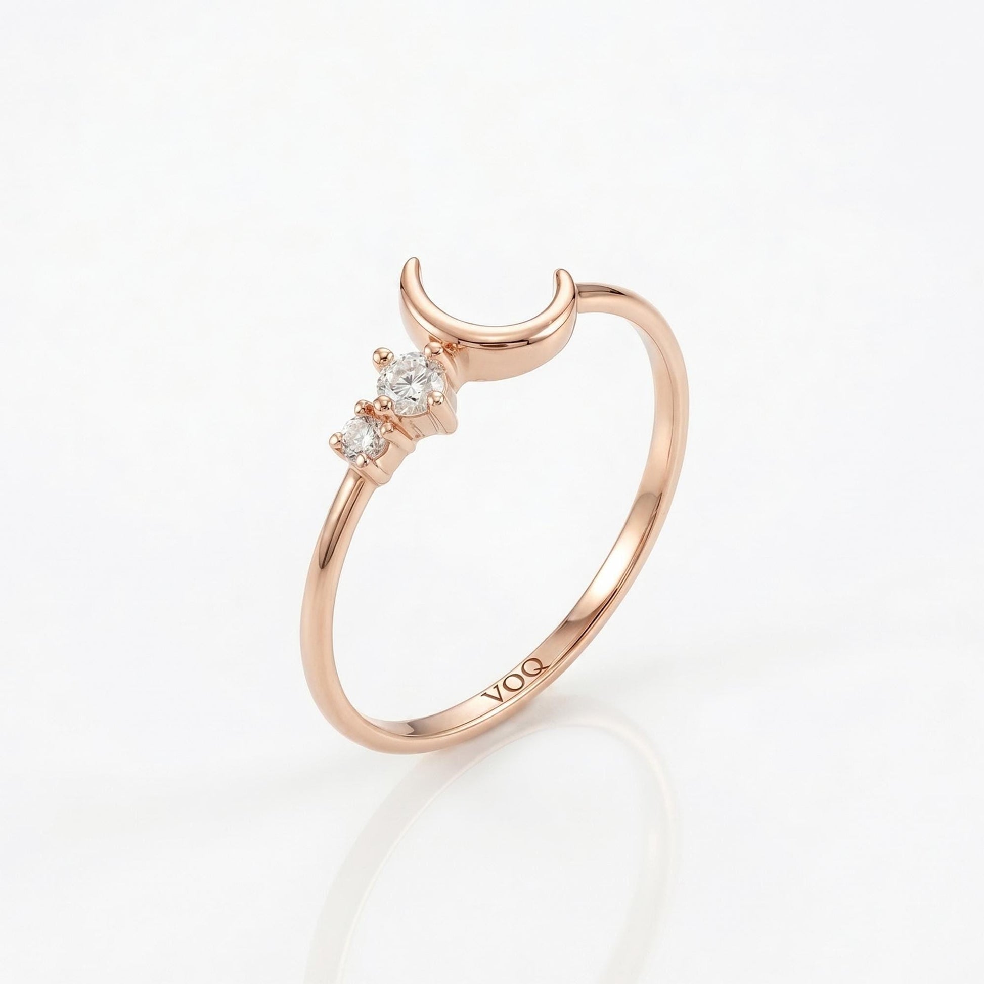 A rose gold ring with a crescent moon and three small diamonds set in the center.