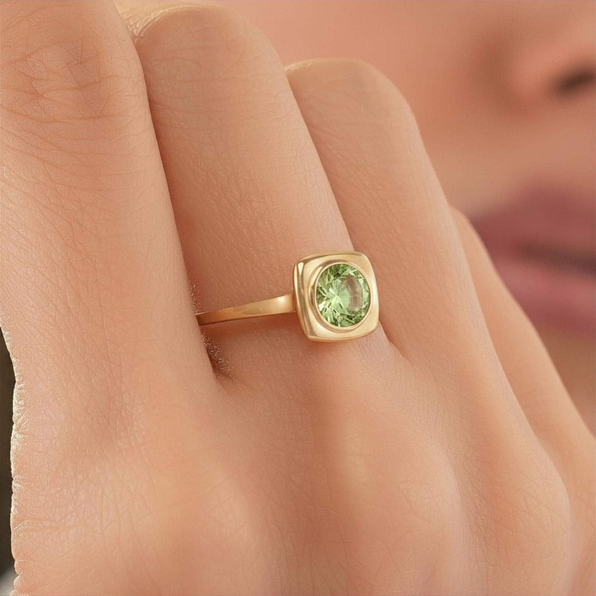 A close-up of a gold ring with a green gemstone on the finger.