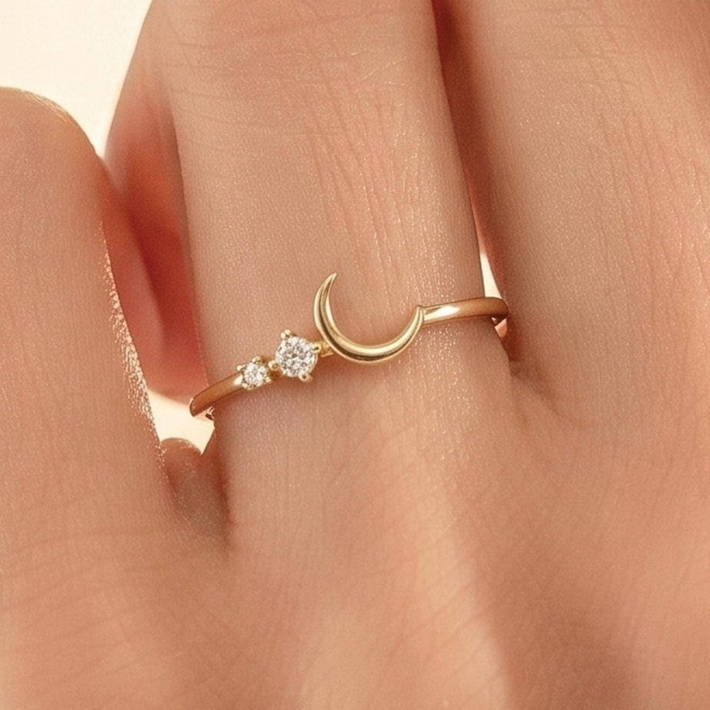A close-up view of a person's hand wearing a gold ring with a crescent moon and two small diamonds.