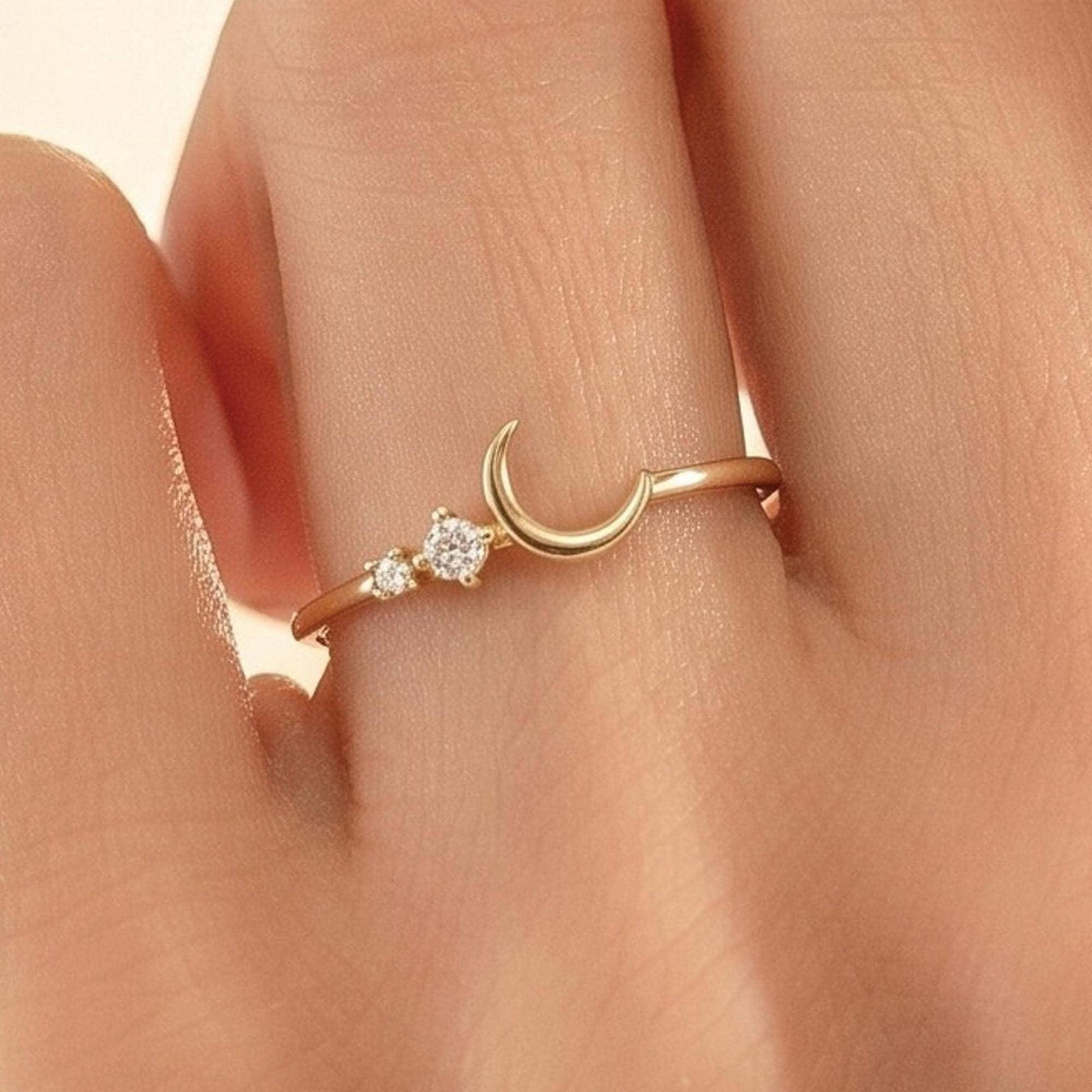 A close-up view of a person's hand wearing a gold ring with a crescent moon and two small diamonds.