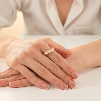 A close-up image of a person's hand wearing a gold ring, resting on a white surface.