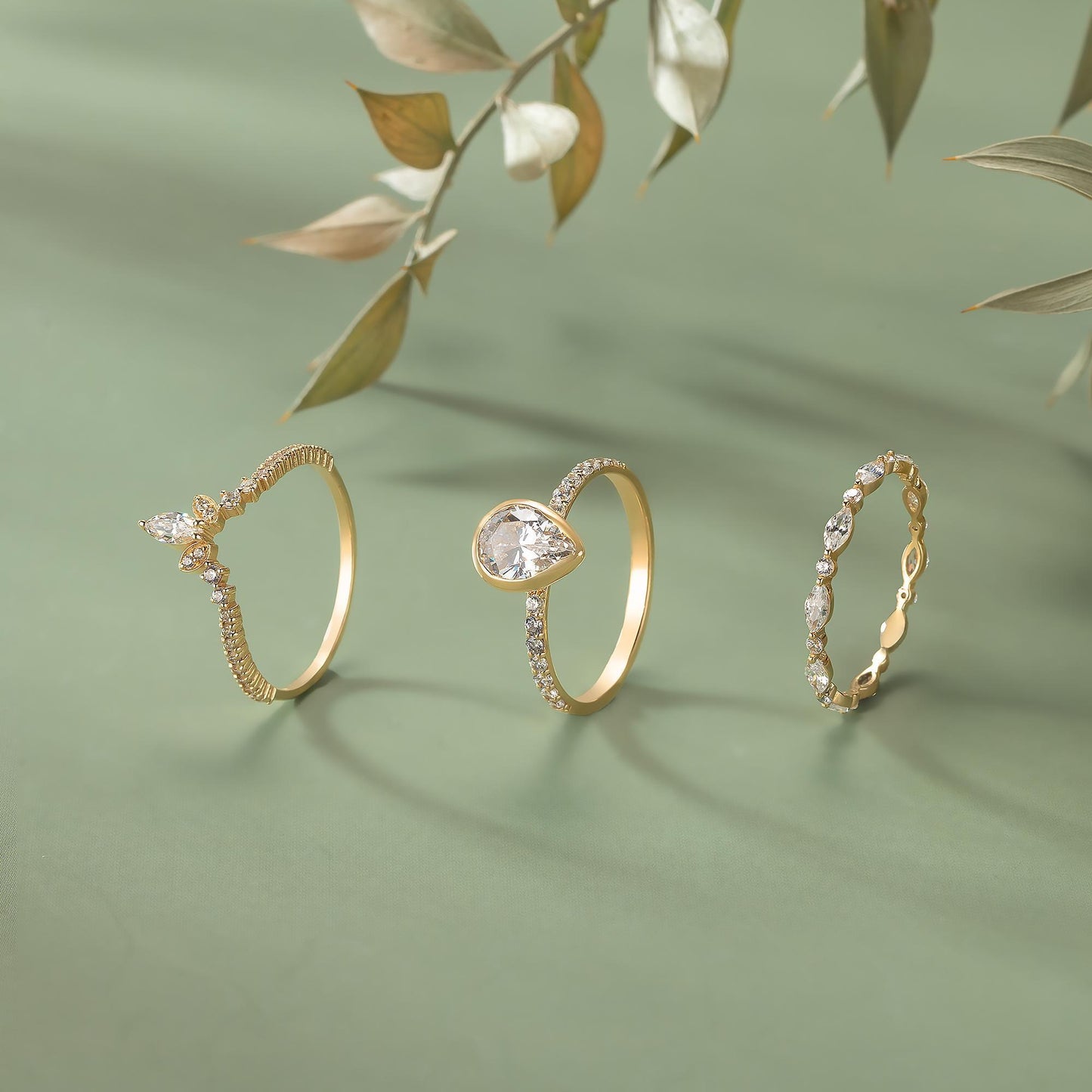 Three gold rings with diamonds are displayed on a green background, with a branch of leaves in the background.