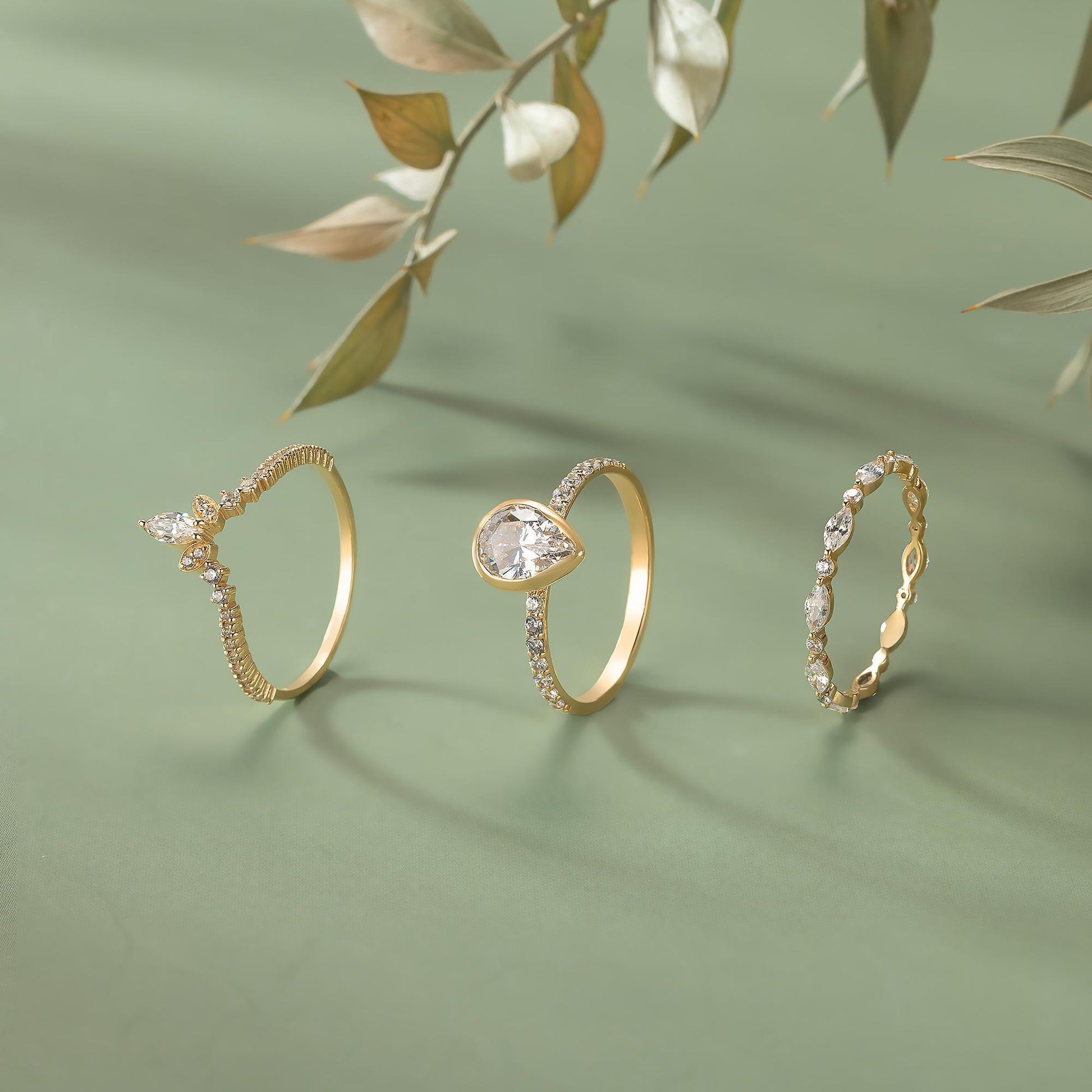 Three gold rings with diamonds are displayed on a green background, with a branch of leaves in the background.