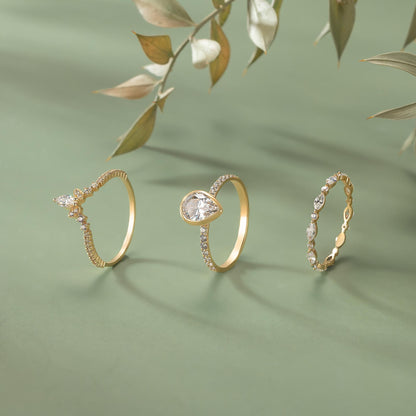 Three gold rings with diamonds are displayed on a green background, with a branch of leaves in the background.