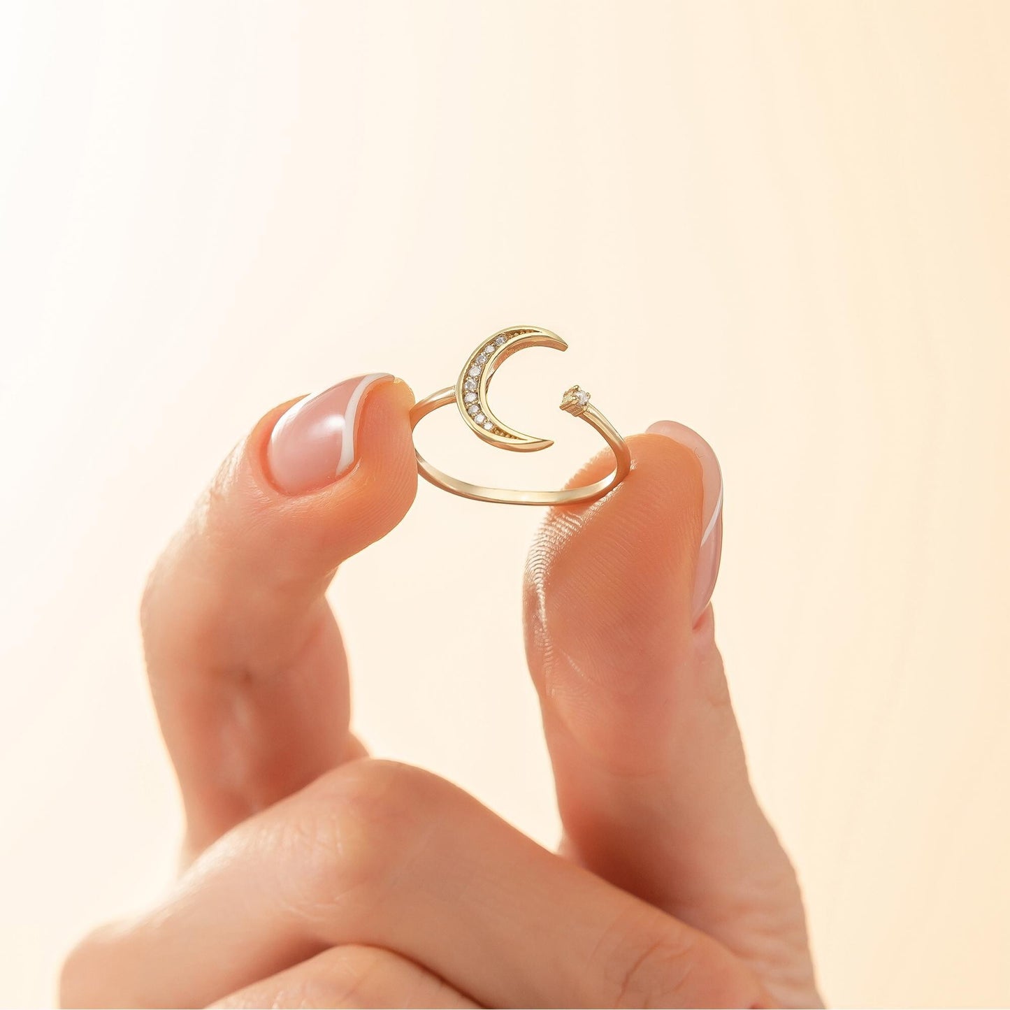 A hand holding a gold ring with a crescent moon design.