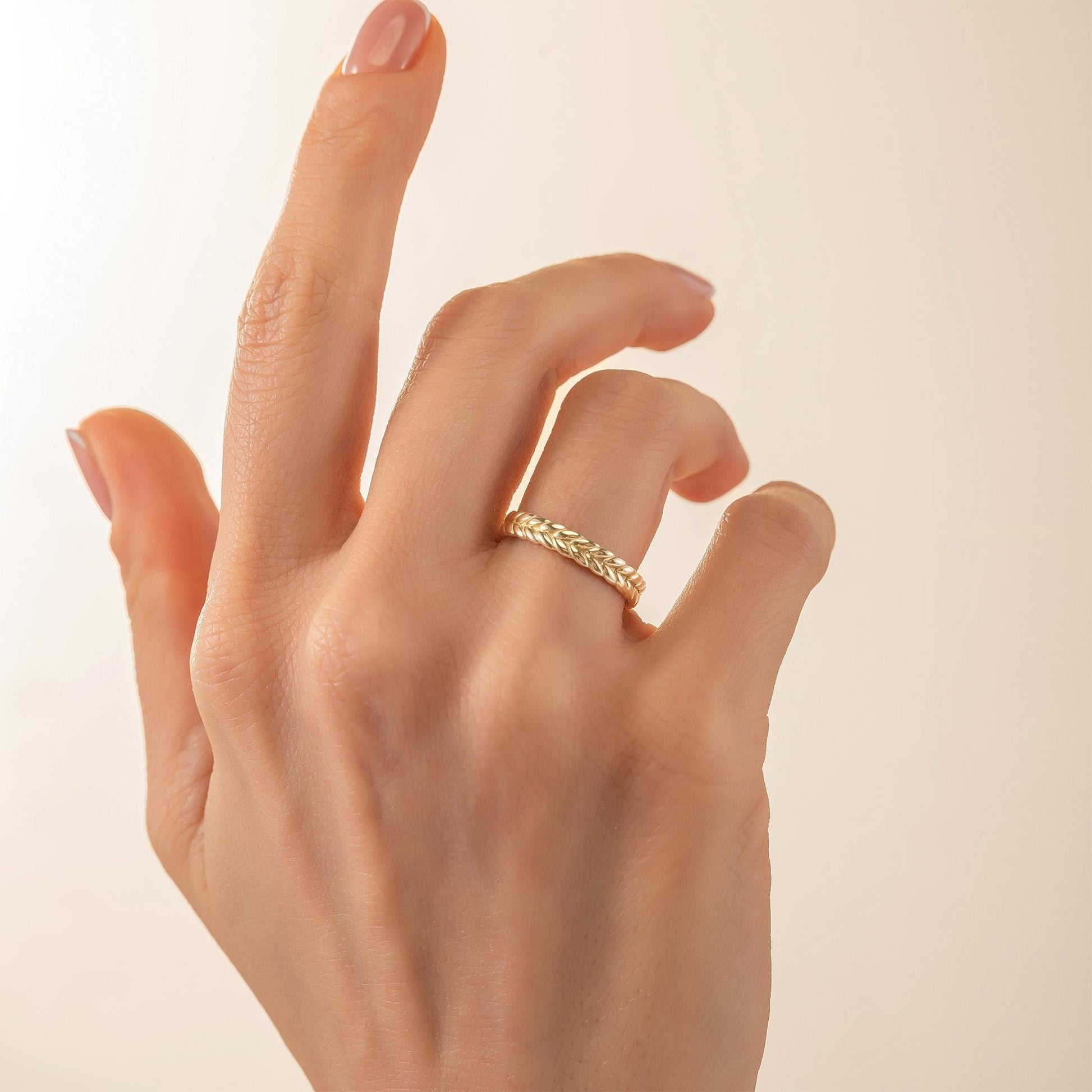 A close-up of a hand wearing a gold ring on the ring finger.