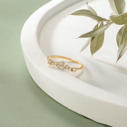 A gold ring with a diamond-encrusted band is displayed on a white pedestal, accompanied by a branch of dried leaves.