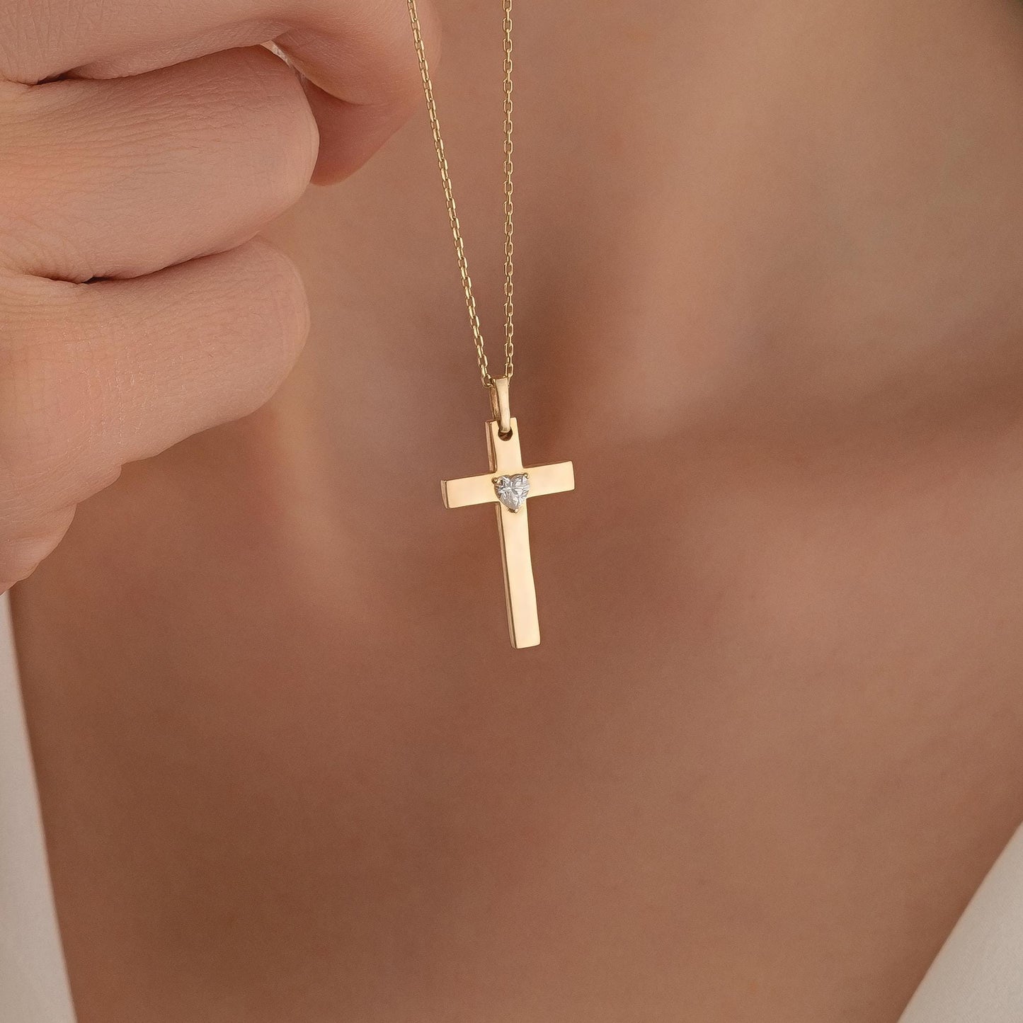 A gold cross pendant with a diamond is being held up by a person's hand.