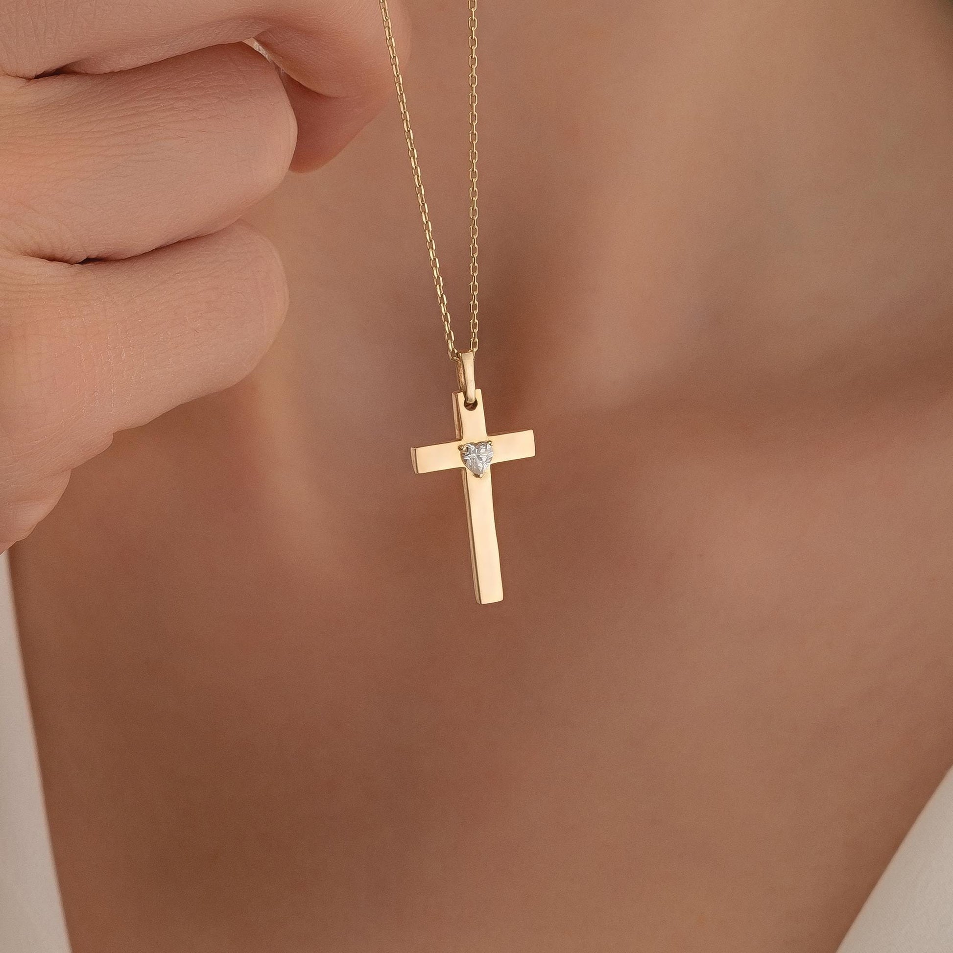 A gold cross pendant with a diamond is being held up by a person's hand.