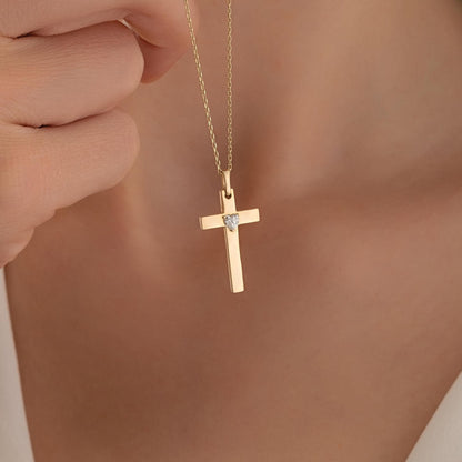 A gold cross pendant with a diamond is being held up by a person's hand.
