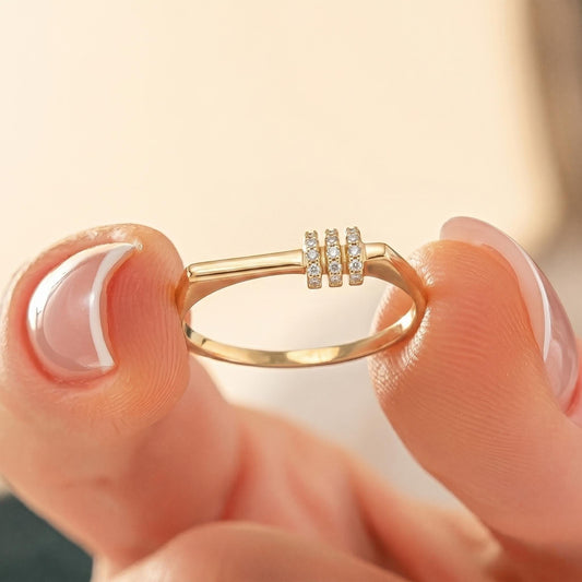 A close-up image of a person's hand holding a gold ring with a small diamond accent.
