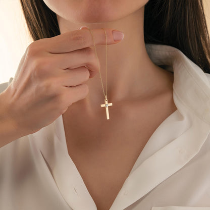 A close-up of a person's neck and chest area, with a gold cross pendant hanging from a chain around their neck.