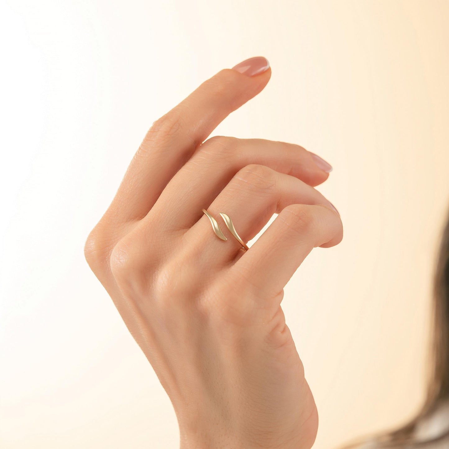 A close-up of a hand wearing a gold ring with a leaf-like design.