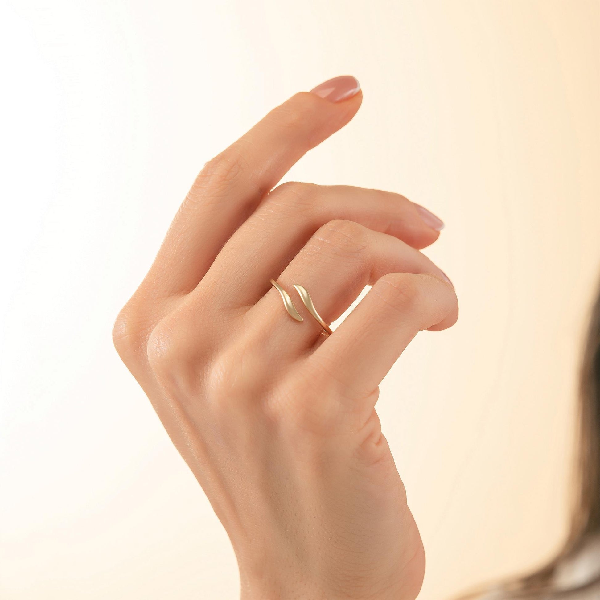 A close-up of a hand wearing a gold ring with a leaf-like design.